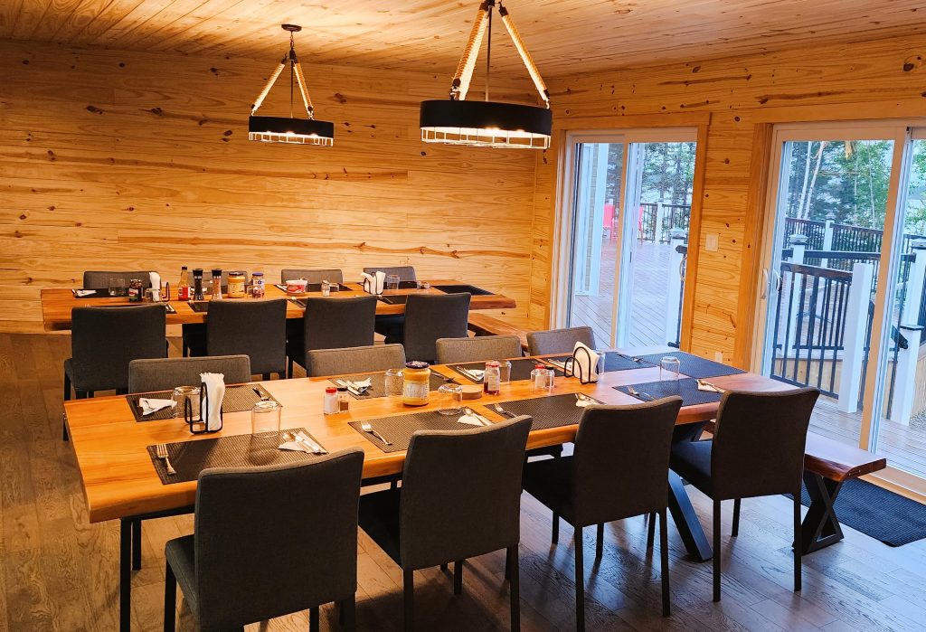 Two large group-friendly dining room tables are set up and ready for a meal, the room has patio doors opening to the beautiful outdoors