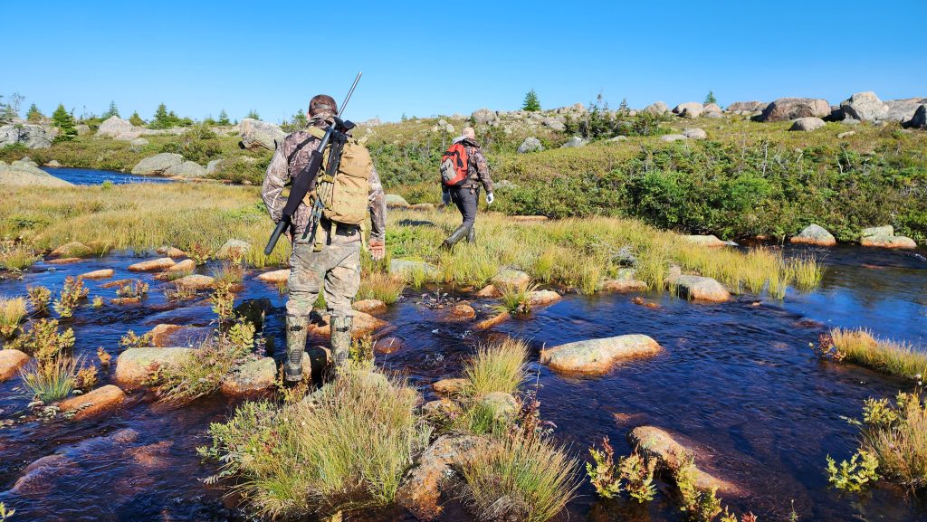 Two men trekking across a river with hunting gear on their backs as they set off into the Newfoundland wilderness in search of big game