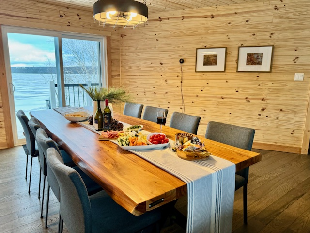A large dining room table is set up with wine and appetizers for a group of Newfoundland Adventures lodge guests. The room has a beautiful lake view.